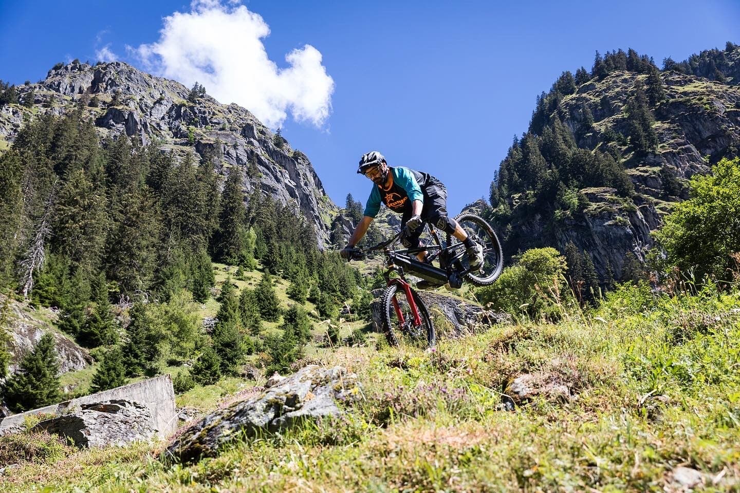 Mountain biker descending beneath alpine crags in summer light